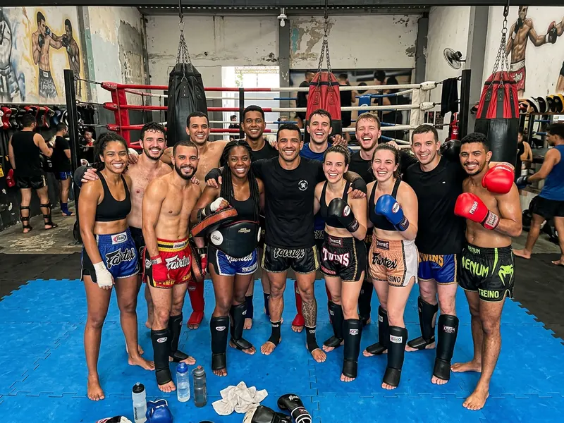 Foto de fim de treino de uma turma de muay thai com luvas e caneleiras na frente do ringue